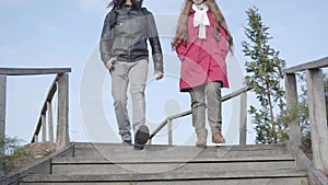 Young middle eastern man and caucasian woman in casual clothes going down the stairs in autumn park. Hippie couple