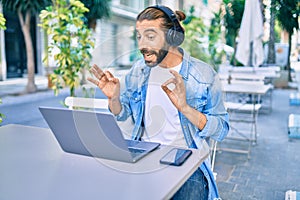 Young middle eastern man doing video call using laptop and headphones at coffee shop terrace