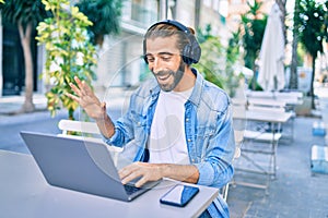 Young middle eastern man doing video call using laptop and headphones at coffee shop terrace