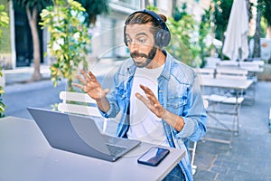 Young middle eastern man doing video call using laptop and headphones at coffee shop terrace