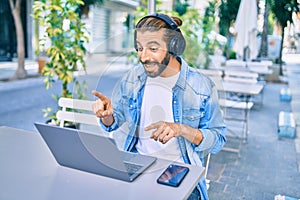 Young middle eastern man doing video call using laptop and headphones at coffee shop terrace