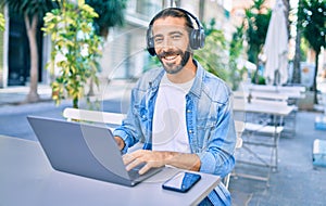 Young middle eastern man working using laptop and headphones at coffee shop terrace
