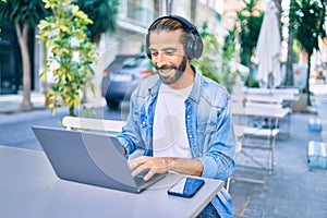 Young middle eastern man working using laptop and headphones at coffee shop terrace