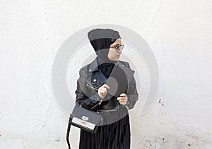 Young middle-eastern student girl holding in hands stack of notepads and her handbag. Modern Muslim woman wearing traditional