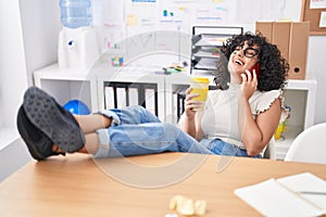 Young middle eastern woman business worker talking on smartphone drinking coffee at office