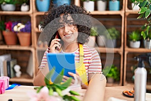 Young middle eastern woman florist talking on smartphone using touchpad at florist