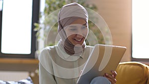 Young middle eastern woman in hijab web surfing in social media on digital tablet, enjoying internet content, free space