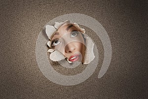 Young Middle eastern woman looking up from ripped paper hole