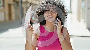 Young middle eastern woman talking on smartphoe using handfan at street