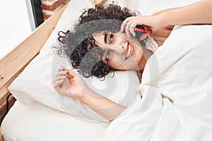 Young middle eastern woman talking on smartphone lying on bed at bedroom