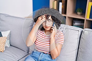 Young middle eastern woman talking on smartphone with worried expression at home