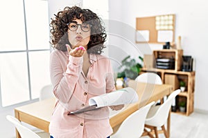 Young middle eastern woman wearing business style at office looking at the camera blowing a kiss with hand on air being lovely and