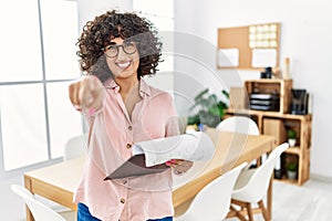 Young middle eastern woman wearing business style at office pointing to you and the camera with fingers, smiling positive and