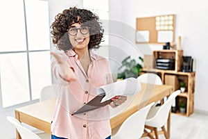 Young middle eastern woman wearing business style at office smiling friendly offering handshake as greeting and welcoming