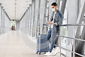 Young Middle Eatern Man In Medical Mask Relaxing With Smartphone In Airport photo