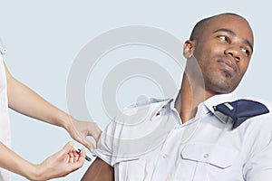 Young military man looking away as being injected by nurse over light blue background