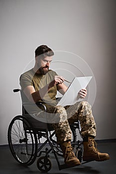 Young military man sitting in a wheelchair and painting on a canvas