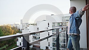 young millenial bold man morning strech on balcony - medium long space copy