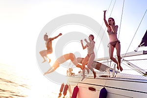 Young millenial friends jumping from sailboat at sea ocean trip - Guys and girls having summer fun together at sail boat party day photo