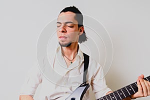 Young millenial man sitting on the floor of home playing an electric guitar