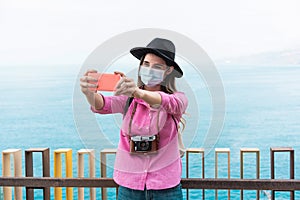 Young millenial woman making a vlog with her smartphone while wearing a protective mask during her travel for coronavirus spread photo
