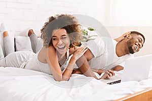 Young black couple lying on bed and using laptop.