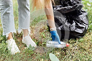 Young millennial caucasian woman cleaning-up public park or forest of plastic garbage. Volunteer picking up plastic