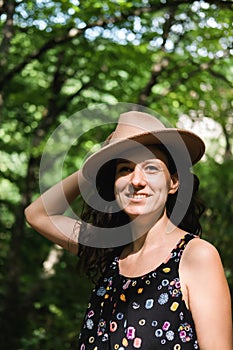 Young millennial woman in dress and beige hat stands in forest happy and relaxed, enjoys nature and tranquility. Travel