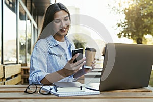 Young millennial woman working in cafe on open terrace, sitting in front of laptop, talking on the phone.