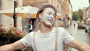 Young mime argues with somebody on street near cafe, then calms down, smiles.