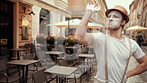 Young mime with bold, cocky look, beckons somebody to fight on street near cafe.