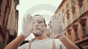 Young mime is hiding behind hands, moving head above imaginary wall.