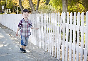 Young Mixed Race Boy Walking with Stick Along White Fence