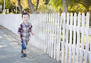 Young Mixed Race Boy Walking with Stick Along White Fence