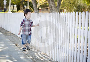 Young Mixed Race Boy Walking with Stick Along White Fence