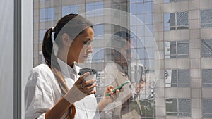 Young Mixed Race Businesswoman Drinking Coffee and Using Mobile Phone in the Office near Big Window with City View at