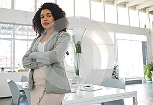 Young mixed race businesswoman standing with her arms crossed while in an office alone. One confident hispanic female