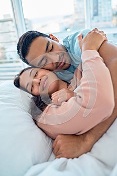 Young mixed race couple lying in bed together and cuddling early in the morning. Handsome asian man holding his