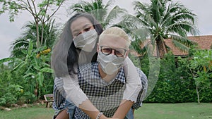 Young mixed race couple wearing protective mask running piggyback and having fun at the home garden