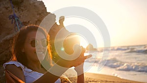 Young Mixed Race Girl Taking Selfie Photo while relaxing in hammock on the beach during amazing sunset. HD Slowmotion.