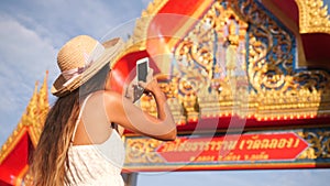 Young Mixed Race Hipster Tourist Girl Taking Photo with Mobile Phone of Thai Buddhist Temple Entrance Gate. Phuket