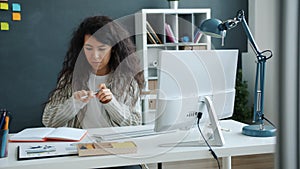 Young mixed race lady working with computer typing then writing info in notebook in office