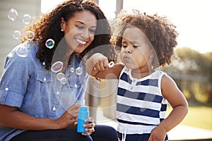 Young mixed race mother and daughter blowing bubbles outside