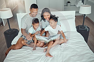 Young mixed race parents mom and dad reading a book to little daughter and son while bonding and spending time together