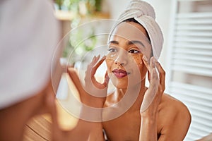 Young mixed race woman applying eye patches in bathroom