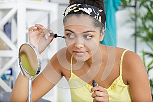 Young mixed-race woman applying mascara