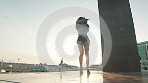 A young mixed race woman with curly hair performing attractive dancing on a background of modern buildings - sunset