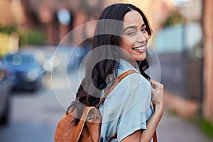 Young mixed race woman with leather backpack walking on urban street