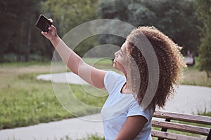 Young mixed race woman looking at smartphone screen, doing selfies, black trendy female enjoying