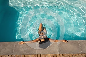 Young mixed-race woman with sunglasses leaning on edge of pool